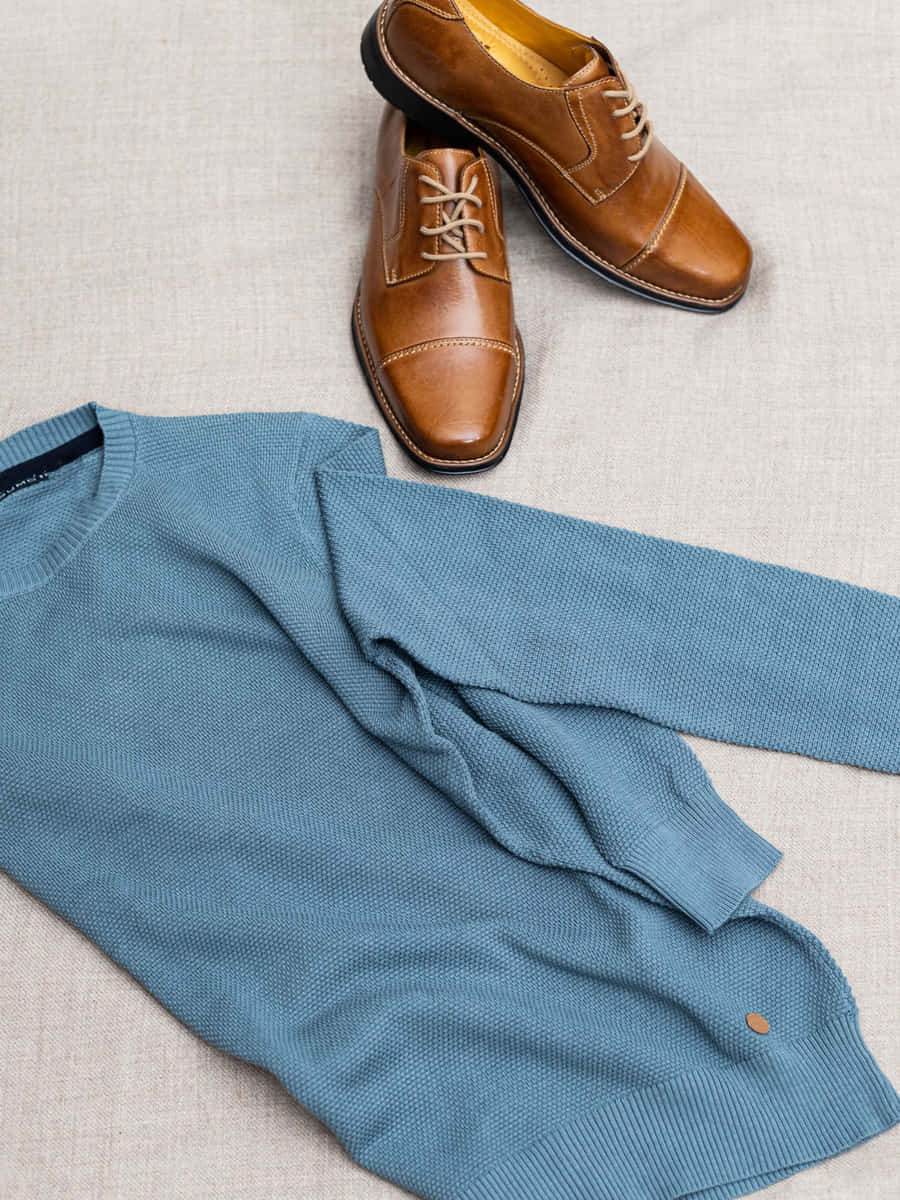 Suéter tejido azul pizarra extendido sobre lino natural, con un par de zapatos de vestir café al lado