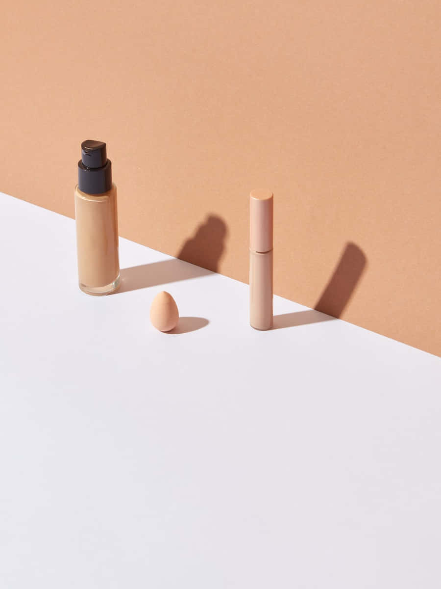 Frasco de base líquida, corrector y esponja de maquillaje de pie sobre un fondo dividido en terracota y blanco