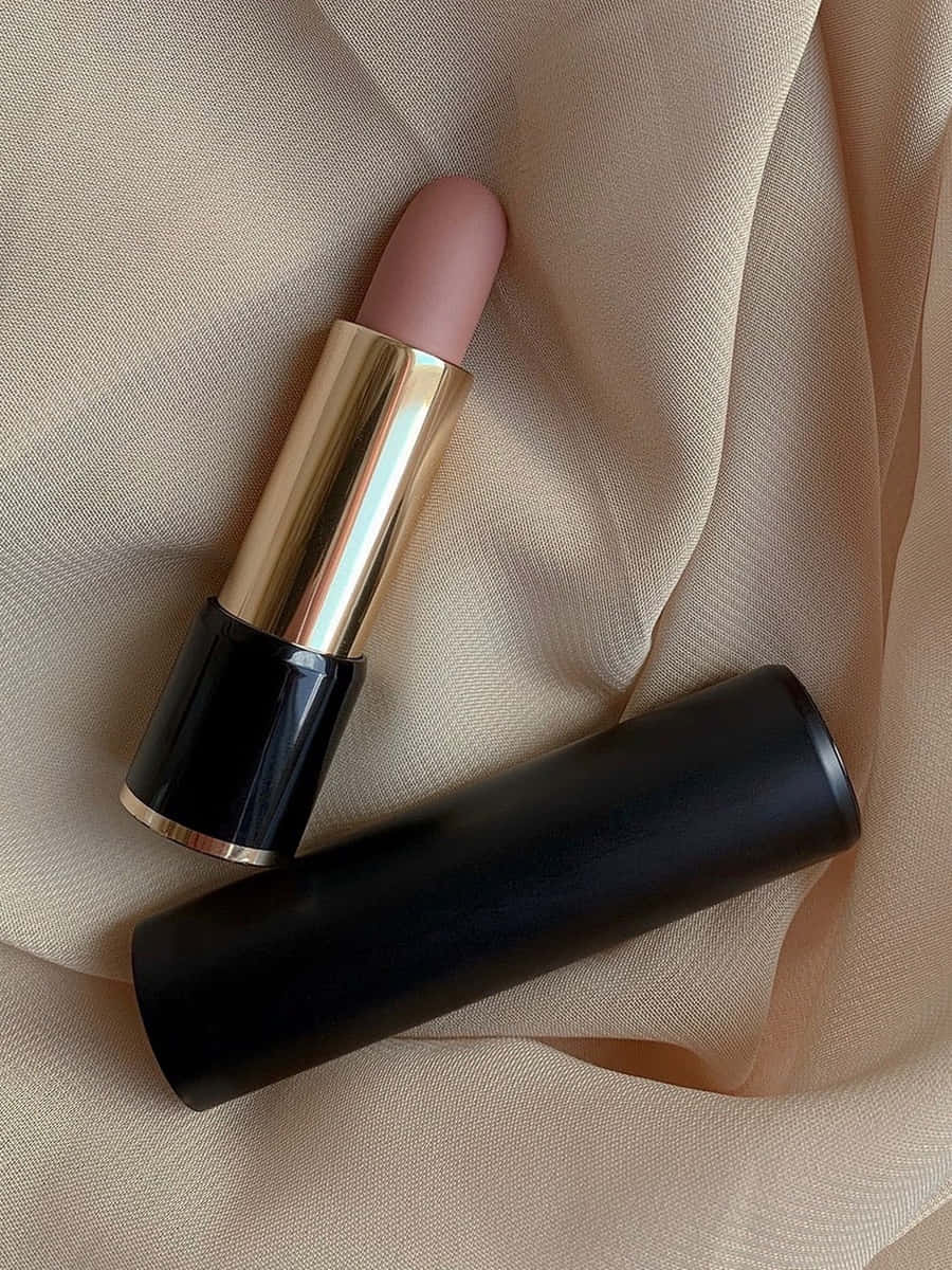 Labial de barra en tono nude rosado, con cuerpo dorado y tapa negra, sobre seda color crema